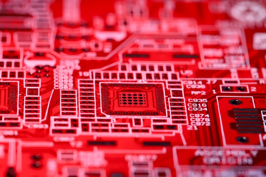 electronic-system-with-electric-circuits-6432109 Detailed macro shot of a red circuit board showcasing electronic components and intricate patterns.